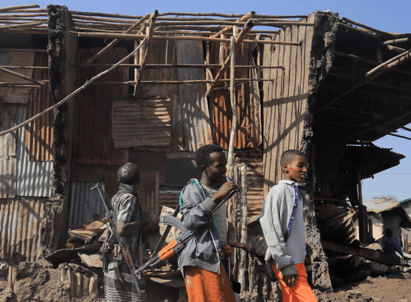 Residents and militias stand next to houses destroyed by an airstrike