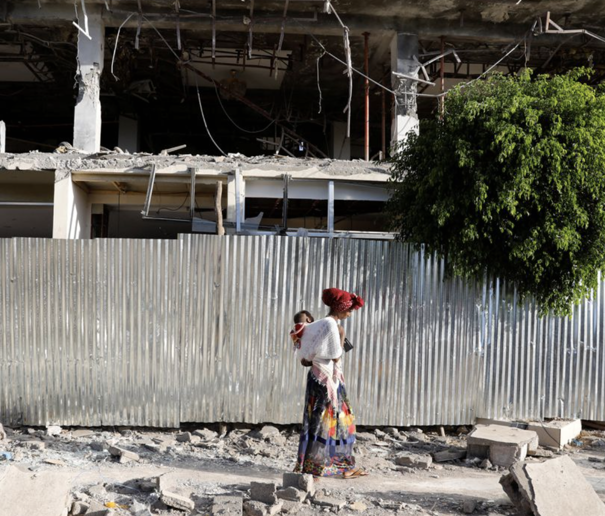 Woman walks past the rubble of a building damaged by fighting in the town of Shire, Tigray region