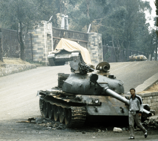Local residents walk past a T-62 main battle tank stranded outside the Presidential Palace following a battle between rebel forces and the government.